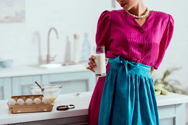 Vista parcial da menina pin up elegante segurando vidro de leite enquanto está perto da mesa da cozinha com produtos diferentes e pó de rosto — Fotografia de Stock