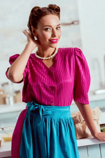 Stylish pin up girl in crimson dress and pearl necklace improving hairdress — Stock Photo