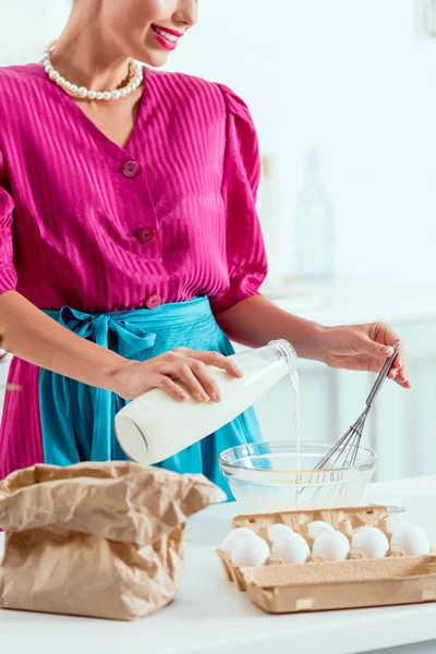 Vista ritagliata della ragazza sorridente pin up aggiungendo latte dalla bottiglia agli ingredienti per fare la pasta — Foto stock