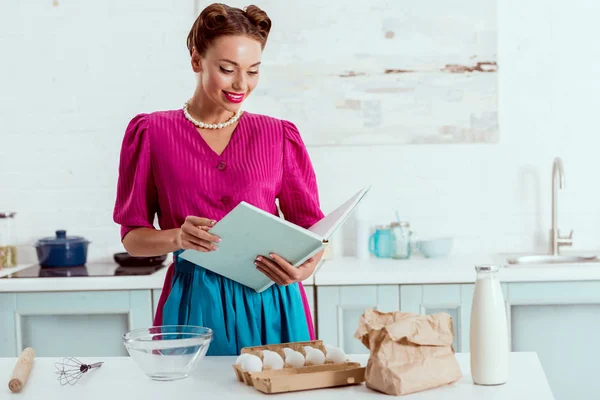 Elegantly dressed pin up girl reading recipes book — Stock Photo