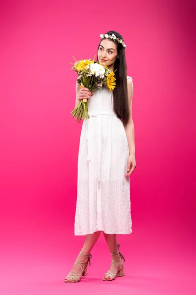Vue pleine longueur de jeune femme heureuse en robe blanche tenant bouquet de fleurs et regardant loin sur rose — Photo de stock