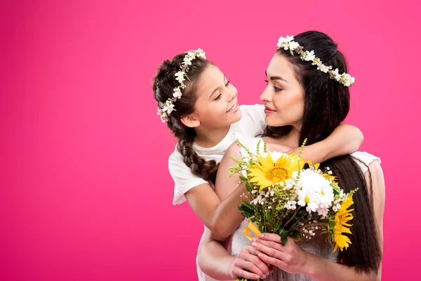 Entzückende glückliche Tochter sieht schöne Mutter mit Blumenstrauß isoliert auf rosa — Stockfoto