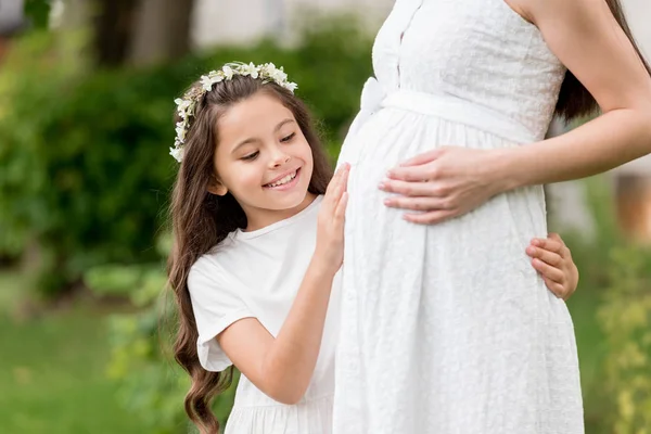 Plan recadré d'adorable enfant heureux dans une couronne florale touchant le ventre de la mère enceinte dans le parc — Photo de stock