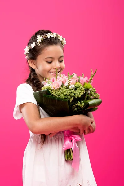 Criança feliz adorável em vestido branco e grinalda floral segurando buquê de flores isolado em rosa — Fotografia de Stock