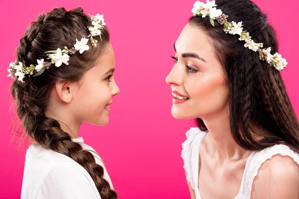 Beautiful happy mother and daughter in white dresses and wreaths smiling each other isolated on pink — Stock Photo