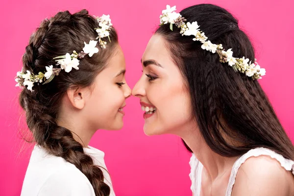 Side view of happy mother and daughter in white dresses and floral wreaths isolated on pink — Stock Photo