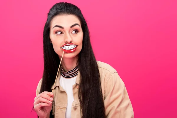 Junge brünette Frau mit lustigen Lippen auf Party-Stick und wegschauen isoliert auf rosa — Stockfoto
