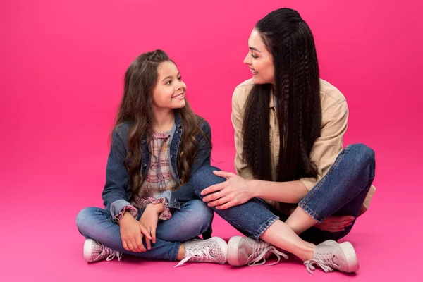 Vista completa de la sonriente madre y su hija sentadas y hablando en rosa - foto de stock