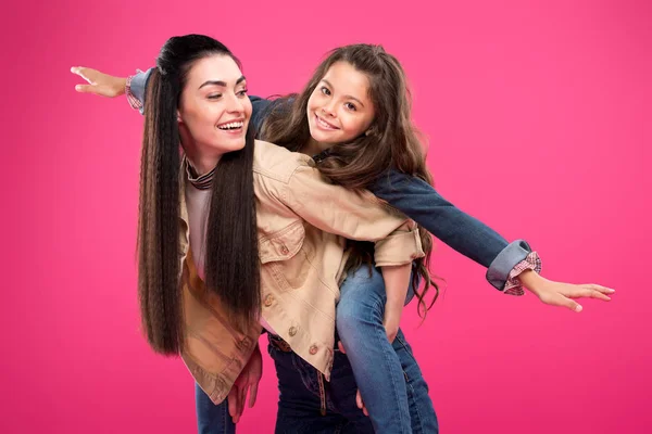 Beautiful happy mother and daughter piggybacking isolated on pink — Stock Photo