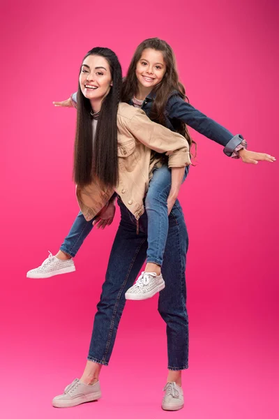 Volle Länge Ansicht der schönen glücklichen Mutter und Tochter huckepack und lächelnd in die Kamera isoliert auf rosa — Stockfoto