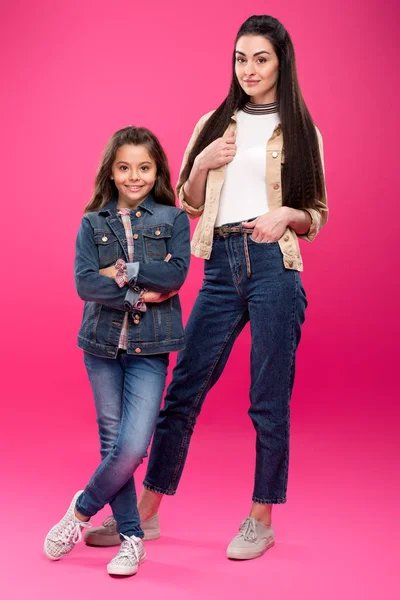 Full length view of beautiful happy mother and daughter standing together and smiling at camera on pink — Stock Photo