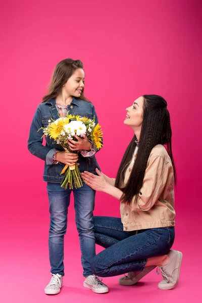 Pleine longueur vue de mère heureuse regardant fille souriante mignonne tenant bouquet de fleurs sur rose — Photo de stock