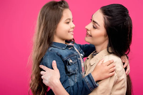 Feliz madre e hija abrazándose y sonriéndose aisladas en rosa - foto de stock