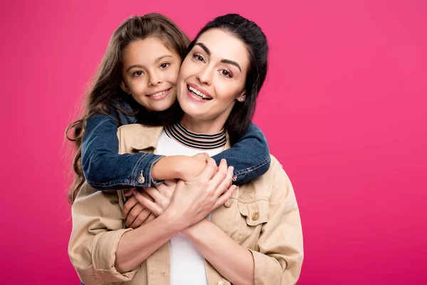 Bella madre felice e figlia abbracciando e sorridendo alla fotocamera isolata su rosa — Foto stock