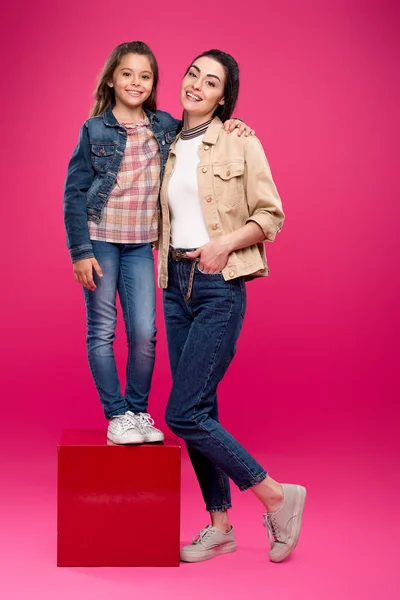 Visão de comprimento total de bela mãe feliz e filha sorrindo para a câmera em rosa — Fotografia de Stock