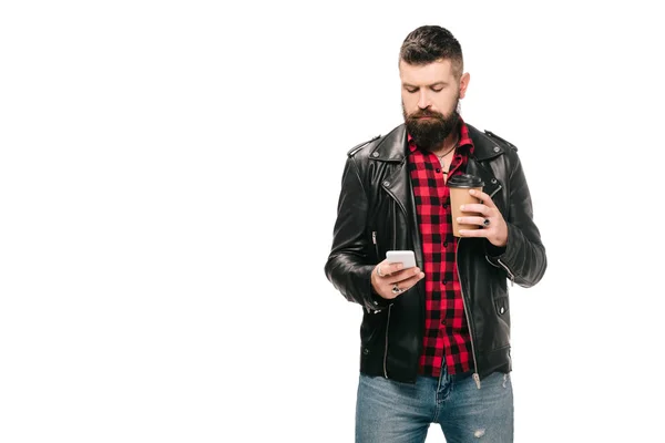 Бородатий чоловік в чорній шкіряній куртці, що тримає каву, щоб піти і використовувати смартфон, ізольований на білому — стокове фото