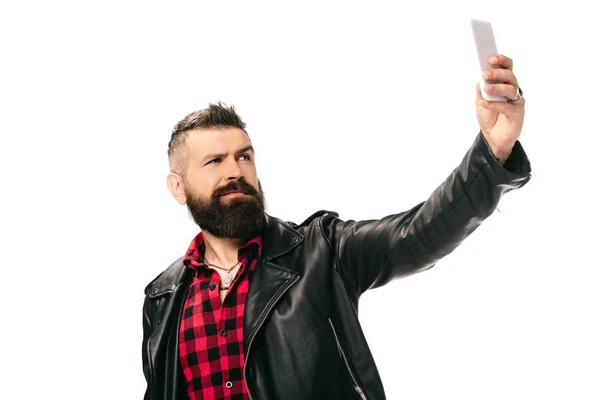 Bel homme barbu en veste en cuir noir prenant selfie sur smartphone, isolé sur blanc — Photo de stock