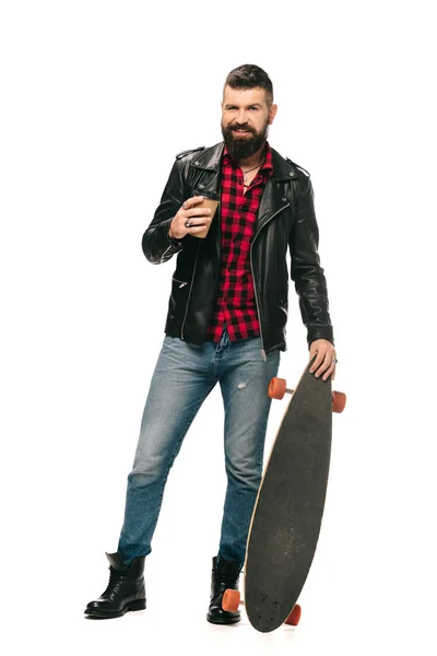 Hombre barbudo en chaqueta de cuero negro posando con longboard y café para ir aislado en blanco - foto de stock