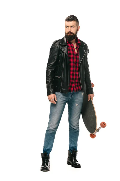 Patinador barbudo em jaqueta de couro preto posando com longboard isolado no branco — Fotografia de Stock