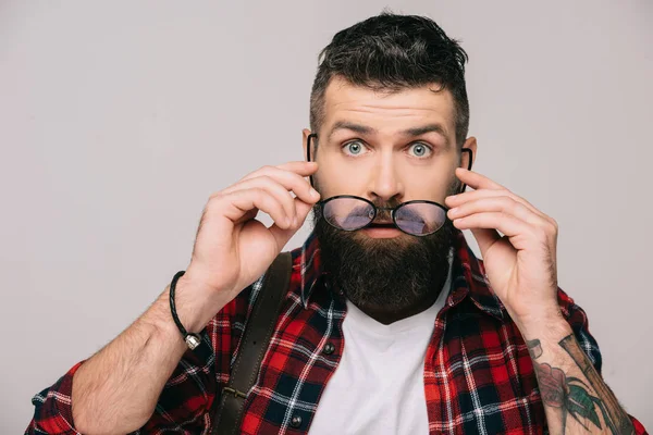 Uomo barbuto sorpreso che tiene gli occhiali, isolato su grigio — Foto stock