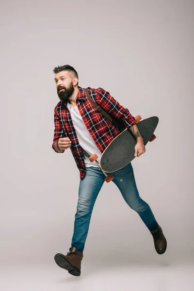 Bonito homem correndo com longboard isolado no cinza — Fotografia de Stock