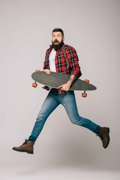 Excited man jumping with longboard isolated on grey — Stock Photo
