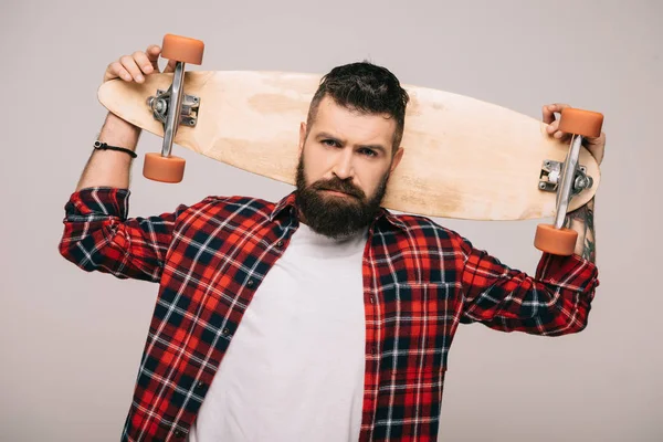 Hombre barbudo guapo en camisa a cuadros posando con longboard aislado en gris - foto de stock