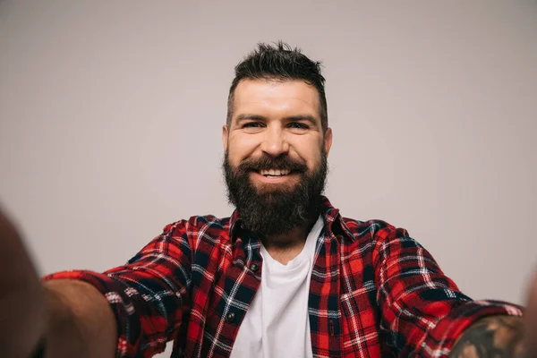 Hombre barbudo alegre en camisa a cuadros tomando selfie, aislado en gris - foto de stock