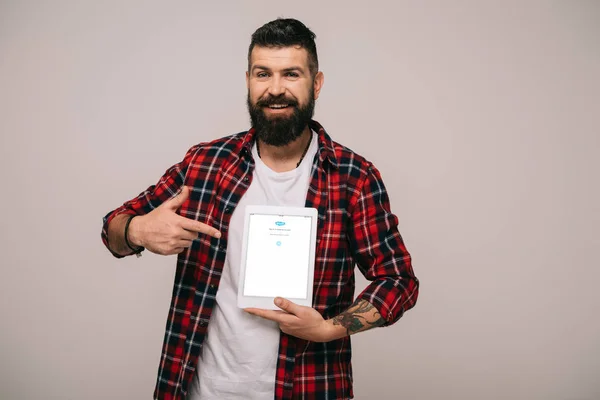 Homem barbudo em camisa quadriculada apontando para tablet digital com aplicativo skype, isolado em cinza — Fotografia de Stock