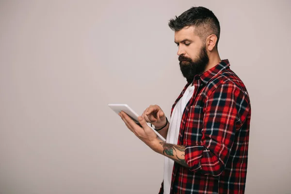 Hombre barbudo guapo en camisa a cuadros usando tableta digital, aislado en gris — Stock Photo