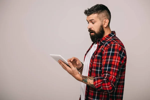 Hombre sorprendido en camisa a cuadros usando tableta digital, aislado en gris - foto de stock