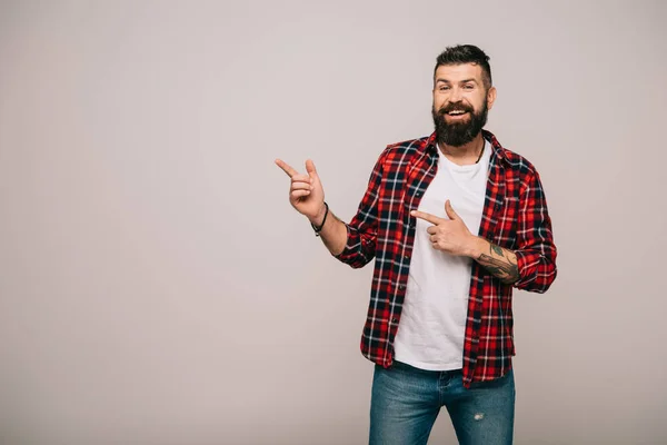 Smiling bearded man in checkered shirt pointing isolated on grey — Stock Photo