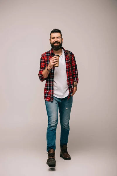Bel homme joyeux en chemise à carreaux tenant café pour aller isolé sur gris — Photo de stock