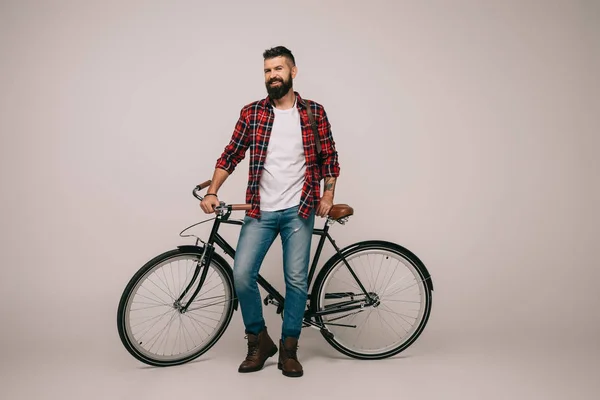 Щасливий чоловік у картатій сорочці позує з велосипедом на сірому — стокове фото