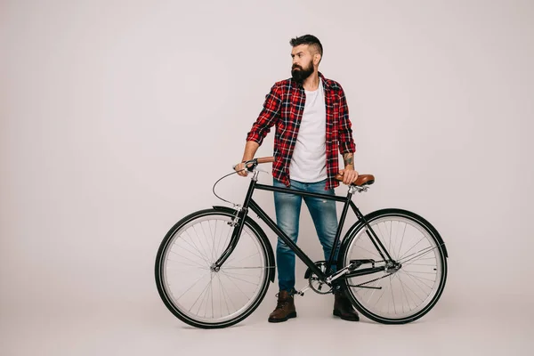Hombre barbudo con camisa a cuadros posando con bicicleta en gris - foto de stock