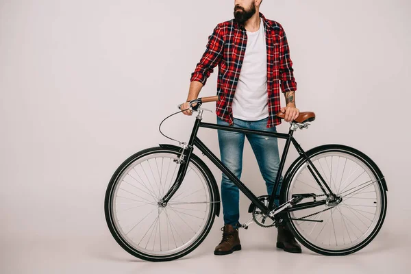 Обрізаний вид чоловіка в картатій сорочці позує з велосипедом на сірому — стокове фото