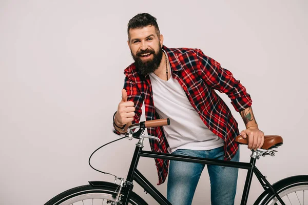 Homme barbu souriant posant avec vélo et montrant pouce vers le haut isolé sur gris — Photo de stock