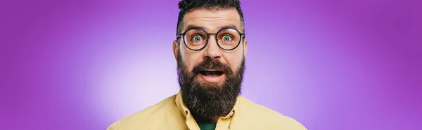 Impactado hombre barbudo en gafas mirando a la cámara, aislado en púrpura - foto de stock