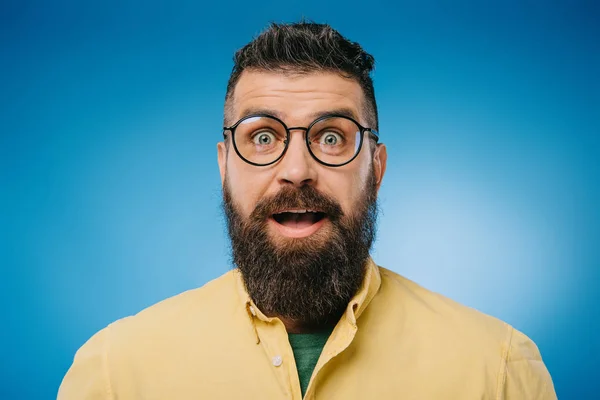Sorprendido barbudo hombre en gafas mirando cámara aislada en azul - foto de stock
