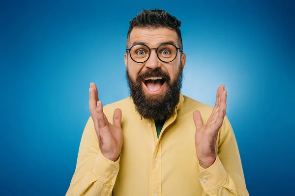 Hombre barbudo excitado en gafas gestos aislados en azul - foto de stock