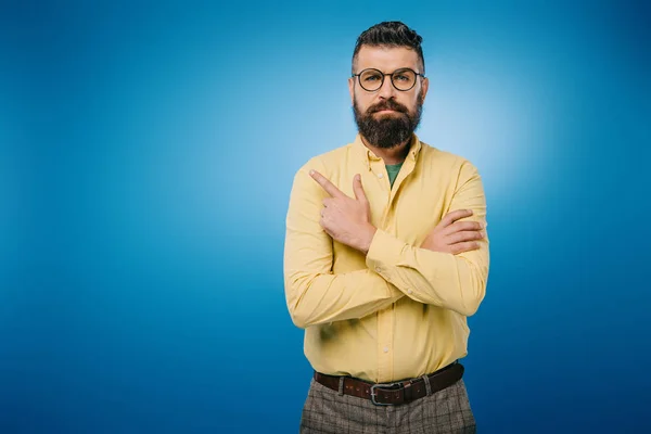 Confident bearded man in eyeglasses pointing isolated on blue — Stock Photo