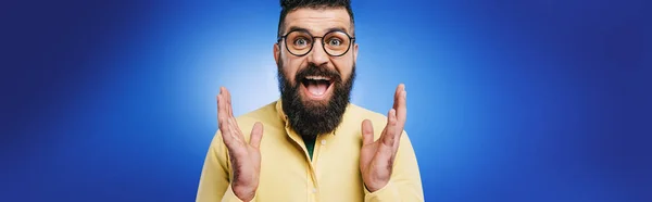 Aufgeregter gutaussehender Mann mit Brille gestikuliert vereinzelt auf blauem Grund — Stockfoto
