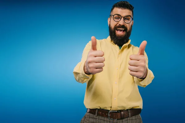 Взволнованный бородатый мужчина в очках показывает большие пальцы вверх изолированы на синий — стоковое фото