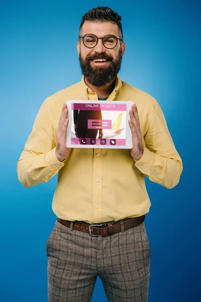 Sonriente hombre barbudo presentando tableta digital con aplicación de boletos en línea, aislado en azul - foto de stock