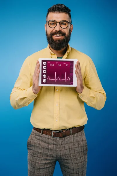Homem barbudo sorridente mostrando tablet digital com dados de saúde, isolado em azul — Fotografia de Stock