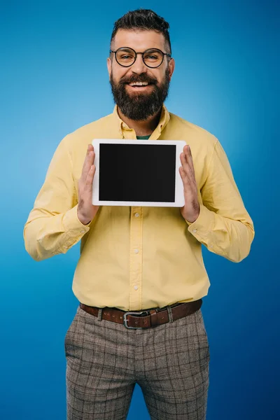 Улыбающийся бородатый мужчина показывает цифровой планшет с чистым экраном, изолированный на синий — стоковое фото