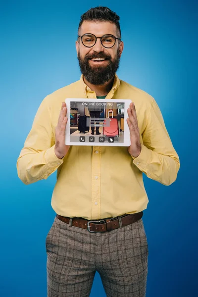 Homem barbudo sorridente apresentando tablet digital com aplicativo de reserva on-line, isolado em azul — Fotografia de Stock