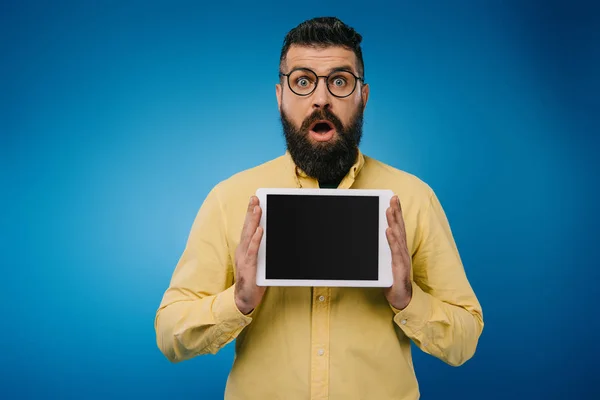 Schockierter Mann zeigt digitales Tablet mit leerem Bildschirm, isoliert auf blauem Grund — Stockfoto