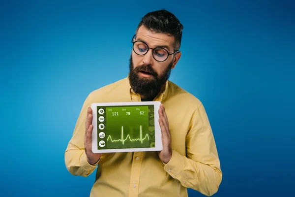 Interessierter bärtiger Mann schaut auf digitales Tablet mit Gesundheitsdaten, isoliert auf blauem Grund — Stockfoto