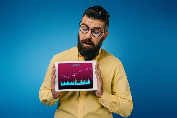 Homem barbudo interessado olhando para tablet digital com aplicativo de tariding, isolado em azul — Fotografia de Stock